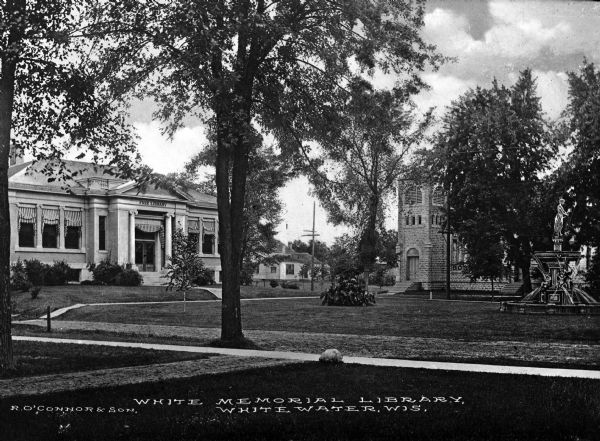 Pathways lead through trees on a lawn to the neo-classical styled White Memorial Library, funded by Mary Flavia White. In front of the library is Birge Fountain, given to the city by Julius Birge in 1903. Caption reads: "White Memorial Library, Whitewater, Wis."