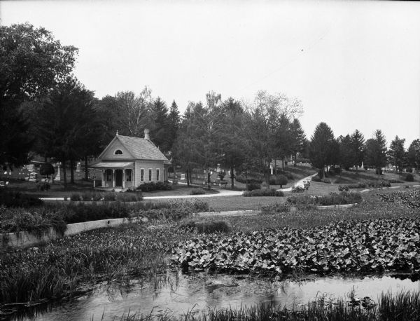 View toward the tombstones and a building at Hillside Cemetery and Park. In the foreground is a pond surrounded by vegetation.