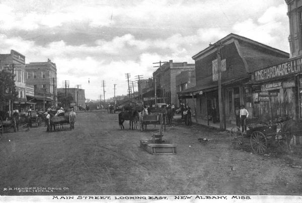 View down Main Street looking east. Signs read: "King Hardware and Lumber" "Fish Bros. Wagon Co." "W.N. Parks" "Mayors Office" and "Coca-Cola." Caption reads: "Main Street, Looking East, New Albany, Miss."