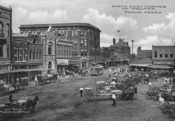 Horse-drawn carts and other wagons in the north corner of a public square. An electric cable car is also visible. Business signs read: "F.C. Robison and Co. Junction Drug Store" "American National Bank" "Thompson and Rodgers Men's Clothing and Furnishings" "Bishop Furniture Co." "George Clark Co." "Eselo 10¢ Cigar" "S.H. Kress & Co." and "Bargan & Ragland." Caption reads: "North East Corner Of Square, Paris, Texas."