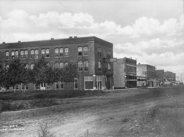 View across unpaved road toward buildings. Business signs read: "Dawson Hotel" and "Afton Furniture Co."