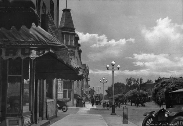 Main Street lined with street lights. Several horse-drawn carts are carrying hay down the street.