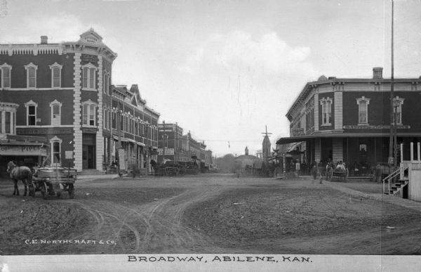 Intersection of unpaved street with horse-drawn carts and storefronts. Business signs read: "Citizens Bank" "Gleissner Druggist" and "Abilene National Bank." Caption reads: "Broadway, Abilene, Kan."