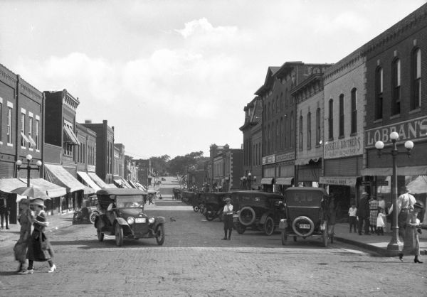 View of Holden Street lined with storefronts, pedestrians and automobiles. Business signs read: "Lobran's" "Russell Brothers Quality Clothes Shop" and "A.A. Grimes Stores Co."
