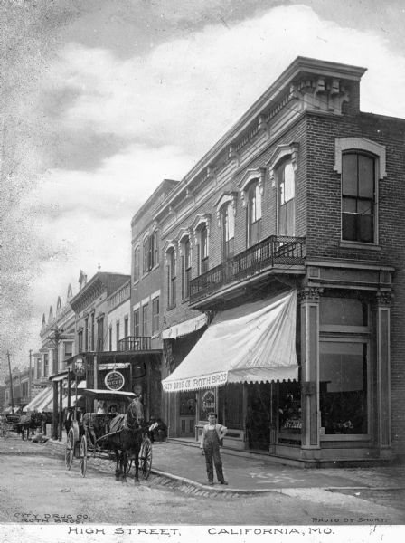 A man stands at an intersection in front of a storefront with a sign that reads: "City Drug Co. Roth Bro.s" Horse-drawn carts are in the street. Other business signs read: "Lemp Beer St. Louis Asahl & Baker" and "Old Lynch Rye." Caption reads: "High Street, California, Mo."