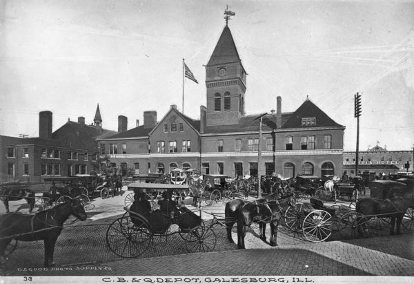 Numerous horse-drawn carriages parked outside the C.B. & Q. Depot. The Columbia Hotel is in the background. Text on top of the building reads: "W. J. Sharp." Caption reads: "C.B. & Q. Depot, Galesburg, Ill."
