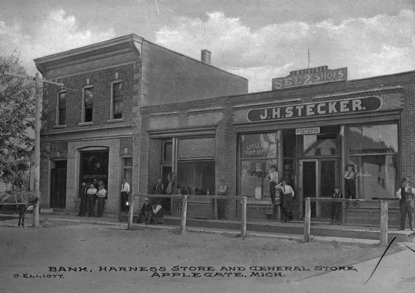 A bank, harness store and general store. Text on building on right side reads: "J.H. Stecker Selz Shoes," "J.H. Stecker" and "Applegate Post Office." Caption reads: "Bank, harness store and general store, Applegate, Mich."