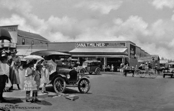 Automobiles, horse-drawn vehicles and pedestrians litter the street. Business signs read: "Dana T. Milner General Merchandise" and "The Bank of Bowie."