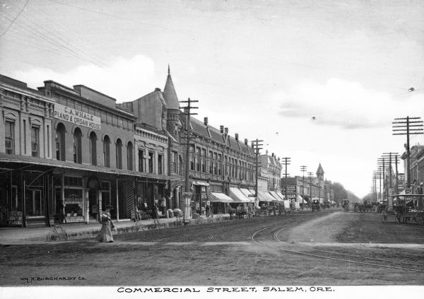 View of Commercial Street. Pedestrians and horse-drawn vehicles are in the street. Business signs read: "C.A. Whale Piano & Organ House" and "Salem Lodging House" (partially obscured). Caption reads: "Commercial Street, Salem, Ore."