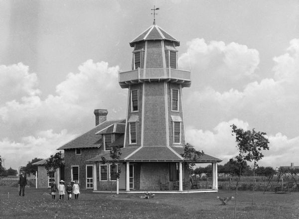 A man and four children stand in front of Edwards Tower Cottage. The cottage is built in the style of a lighthouse.