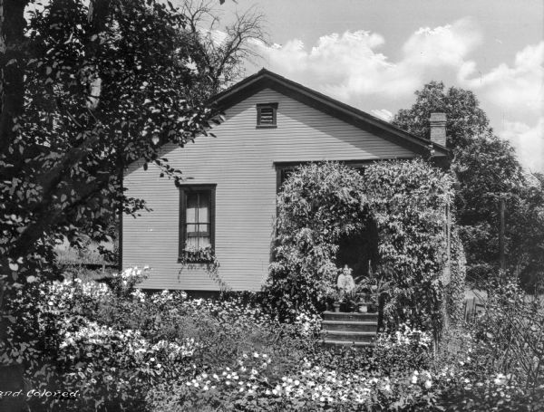 A girl sits on the steps of a small home surrounded by a lush garden. Fairmont was a company town of Consolidated Coal Company.