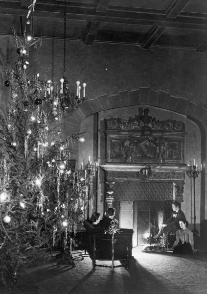 A view of the YWCA lounge at Christmas. Four women and a dog sit in front of an ornate fireplace. A large Christmas tree stands to the left of the fireplace.