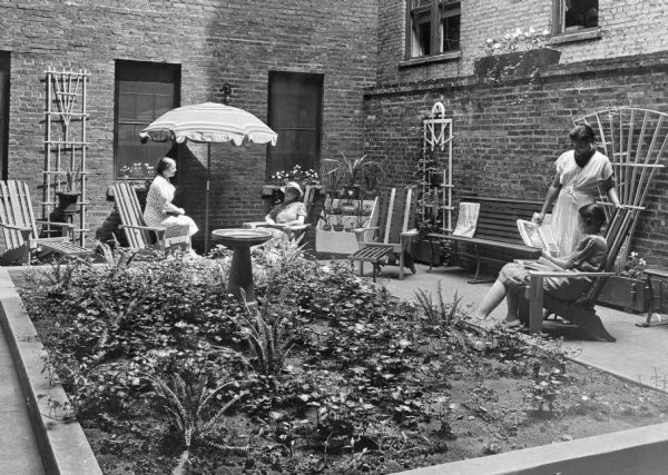 Four African-American women read and enjoy the outdoor patio at the YWCA. The brick patio area features a small garden with a birdbath.