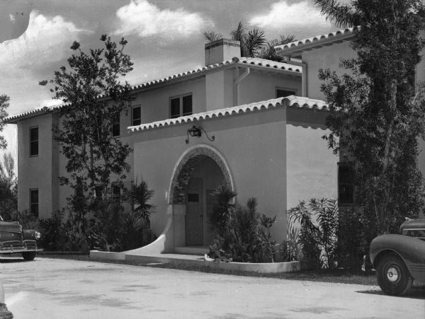 View of the Idlewild Apartments. Two cars are parked outside of the arched entrance to the Spanish adobe apartment house.