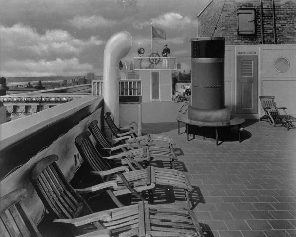 London Terrace marine deck. View of a roofdeck sun porch resembling a ship deck at London Terrace apartments. A man and a woman lounge while a man in a captain's uniform looks on. The apartment complex was completed in 1931 and was considered the largest apartment building in the world. It still stands and occupies the block between 23rd and 24th streets and Ninth and Tenth avenue in West Chelsea in New York City.