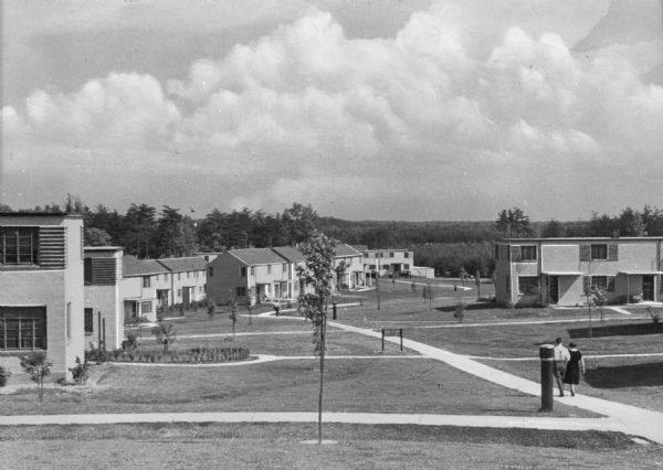 Housing development. A man and a woman walk on the sidewalk in a tidy housing development. Greenbelt was one of three planned communities along with Greendale, Wisconsin and Greenhills, Ohio, designed and implemented by the U.S. Department of Agriculture.