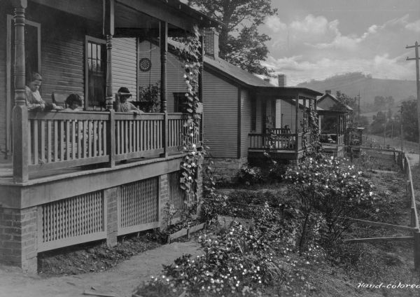Several people sit on the porches of a row of homes in a company town of Consolidated Coal Company.
