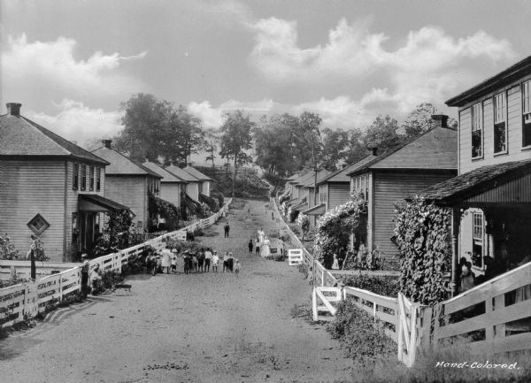 Children and adults stand in an unpaved rural street lined with homes in a company town of Consolidated Coal Company.