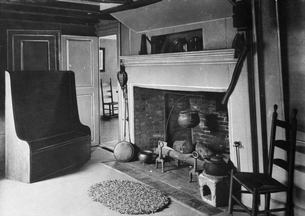 View of kitchen fireplace in Howland House. The Howland House was built in 1667 and still stands. It is also known as the Jabez Howland House and is the only surviving house known to have been occupied by a Mayflower passenger, John Howland. Today it is a museum. View of fireplace with antique kettles, tools and bed warmer, and antique bench and Shaker style chairs.