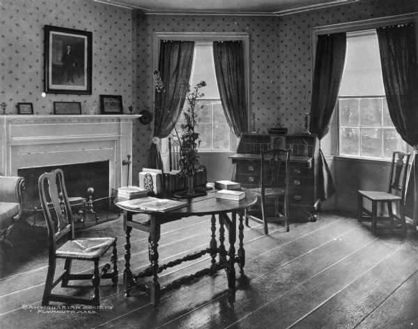View of study interior, antiquarian house. Room features a fireplace and mantle, portrait, a desk, several Shaker style chairs, a table and a settee. Caption reads: "© Antiquarian Society Plymouth, Mass."