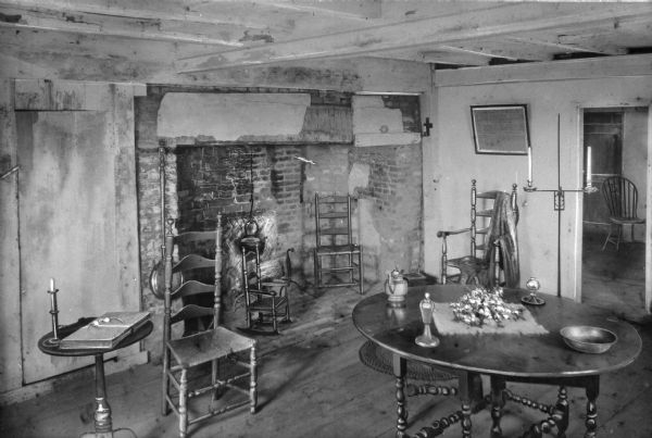 View of the keeping room in the Jethro Coffin home. Jethro Coffin was a blacksmith and the grandson of one of the island's first white settlers, Tristam Coffin. Built in 1686 the house remains the oldest house on Nantucket. Room features a brick fireplace, table, several Shaker-style chairs and a child's Shaker-style chair. A hanging kettle is in the fireplace, and a bedwarmer is next to the fireplace.