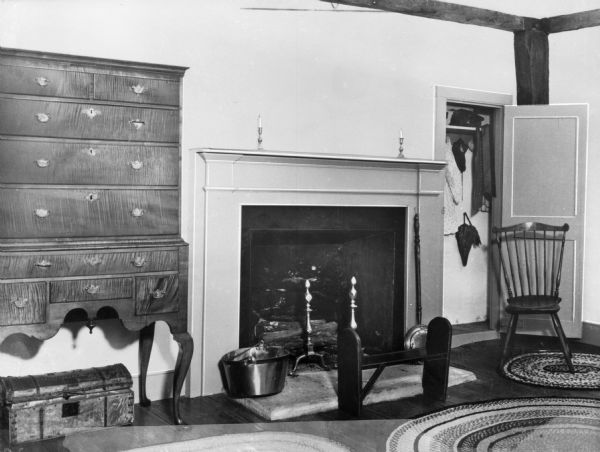 View of a bedroom in the Denison homestead.  The room features an antique highboy dresser, trunk, rugs, fireplace with mantle, wooden bench and chair, and open closet. Built in 1717, the home is a museum today.
