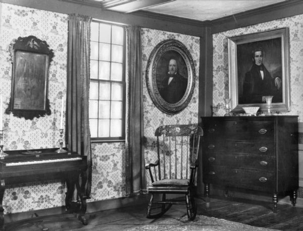 View of formal parlor in Deniston homestead. Built in 1717, the home is a museum today. The room features two formal portraits, a rocking chair, dresser, mirror and a small organ.