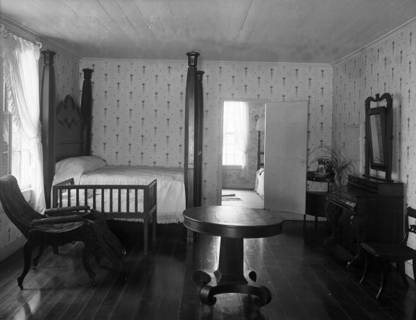 View of a bedroom, located on the campus of Clemson University in Clemson, South Carolina. Fort Hill was the home of John C. Calhoun, who was active in government both in South Carolina and nationally, serving as vice president under John Quincy Adams. The room features a bed, crib, reclining chair, dresser, chair, table and a small corner table. Another bedroom is in the background through a doorway.
