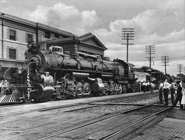 View of the Santa Fe demonstration train number 3009. Spectators are around the train. A sign on the train reads: "A.T. & S.F." and "Santa Fe Type Mallet Articulated (illegible) Largest Locomotive In The World Built At Topeka Shops" (rest illegible).