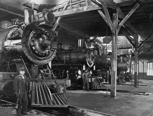 Railroad workers pose near train engines lined up in a wooden roundhouse garage facility. The number on the train in the foreground is "1252."