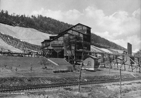 View of the P & R coal storage yard, including railroad tracks and coal storage building. Hills are in the background.