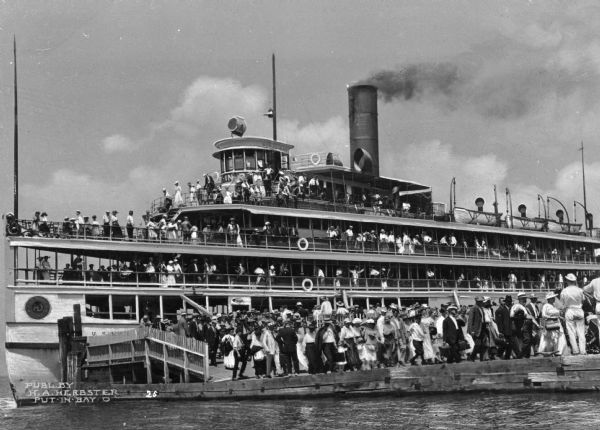 View of tourists arriving on steamship. Many passengers are on the ship and the dock.