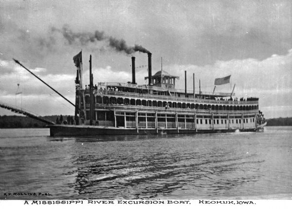 View of the steamship "J.S." in the Mississippi River near Keokuk. Passengers are on board the ship decks, and the initials "J.S." are on the top portion of the ship. Caption reads: "A Mississippi River Excursion Boat Keokuk, Iowa." The ship burned and sank near Victory, Wisconsin on its way to La Crosse, Wisconsin on June 25th, 1910.