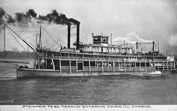 View of the steamship "Fred Herold" in the Mississippi River near Cairo. "Fred Herold" is painted on the ship, and "Lee Line St. Louis & Memphis" is painted near the front of the ship. A large bust sculpture is near the top of the ship. Caption reads: "Steamer "Fred Herold" entering Cairo, Ill. harbor."