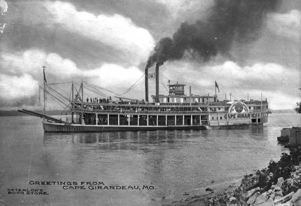 View of the steamboat "Cape Girardeau" in the Mississippi River near Cape Girardeau. Many passengers are on the ship decks. The sign on the ship reads: "South East Mo. Drummers Assn S.E.M.O. D.A." and "Cape Girardeau." Caption reads: "Greetings From Cape Girardeau, Mo."