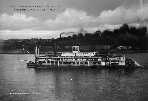 Elevated view of the steamboat "Keystone State" in the Ohio River near Portsmouth. The text "Keystone State" is painted on the rear of the ship, but is partially obscured. The town is in the background. Text on photograph reads: "The "Keystone State" Portsmouth, Ohio."
