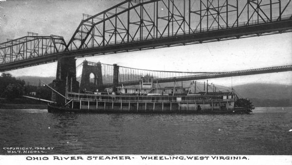 View of the steamboat "Virginia" underneath a bridge in the Ohio River near Wheeling. "Virginia" is painted on the rear of the ship. A second bridge is in the background. Caption reads: "Ohio River Steamer - Wheeling, West Virginia."