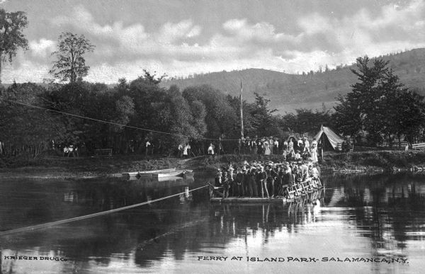 View of the ferry carrying passengers across the Allegheny River near Salamanca, New York's Island Park. Many passengers are on board the ferry, and in the background more people are on shore near a tent. Caption reads: "Ferry at Island Park — Salamanca, NY."