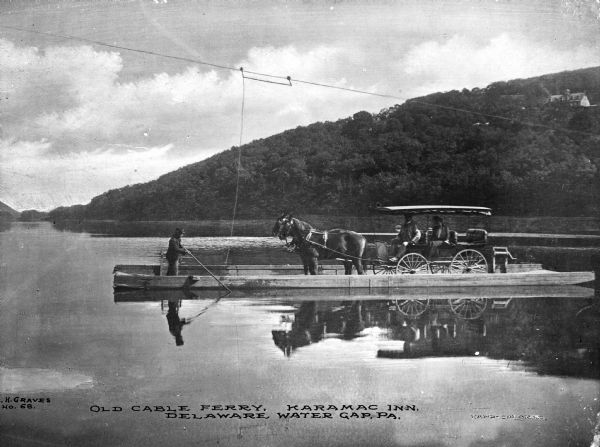 View of a cable ferry, near the Karamac Inn, carrying a horse-drawn vehicle and passengers across the Delaware Water Gap. The shoreline is in the background. Caption reads: "Old Cable Ferry, Karamac Inn. Delaware Water Gap, PA."