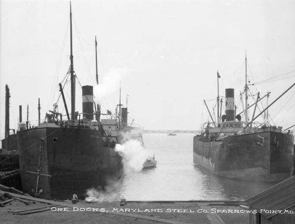 View of several ships at the ore docks of Maryland Steel Company. Text on the ship on the left may read "Craigeab" (text is difficult to make out). The name on the ship on the right reads: "Winifred." Text on photograph reads: "Ore Docks, Maryland Steel Co. Sparrows Point, MD."
