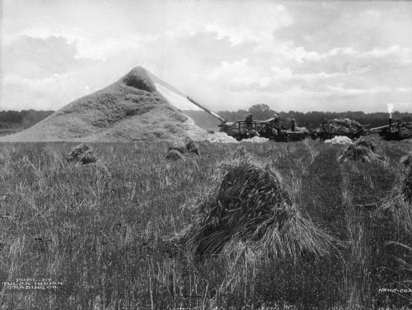 Agricultural workers are shown threshing wheat in a field in the vicinity of Tulsa. The processed wheat is being piled near the equipment. The machine nearest the pile of wheat reads: "Case."