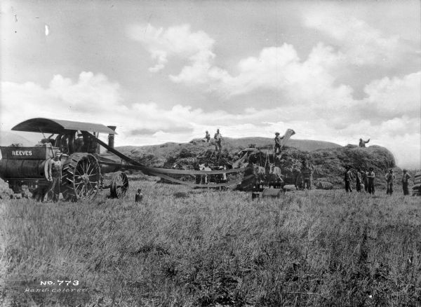 Agricultural workers are shown harvesting grain in the vicinity of Madill. Horse-drawn wagons full of grain are near a large pile of grain. Harvesting or threshing machinery reading "Reeves" is nearby.