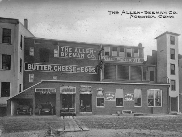 Exterior view of the Allen-Beeman Company. Text on the building reads "Public Warehouse," "Butter, Cheese and Eggs," "Office" "Engineers Dept." "Power House." There are automobiles parked in garages and there are two other entry ways for "Shipping" and "Receiving." Caption reads: "The Allen-Beeman Co., Norwich, Conn."
