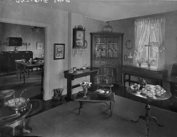 Interior view of an antique shop, the proprietor of which was Mrs. L.H. Morrison. Scene  includes teacups on saucers, a wooden chair, an oil lamp, a table and chairs, and a number of other odds and ends that would generally be found in an antique store.