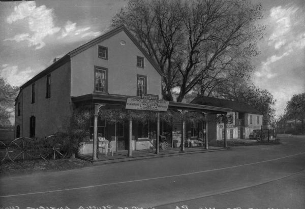 Exterior view of an antique shop. Signage reads, "Post Office, King of Prussia, Furniture, Antique Shop, Old Glass, L.H. Morrison." Also visible are chairs on the front porch and a fence made of wagon wheels.