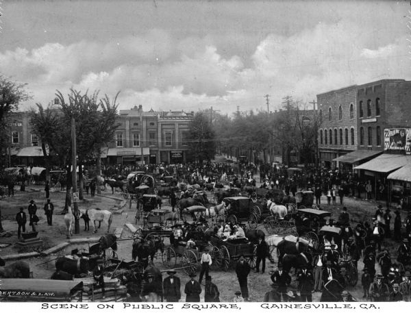A large number of men with horse-drawn carts gathering in a public square for Market Day. Caption reads: "Scene on Public Square, Gainesville, GA."