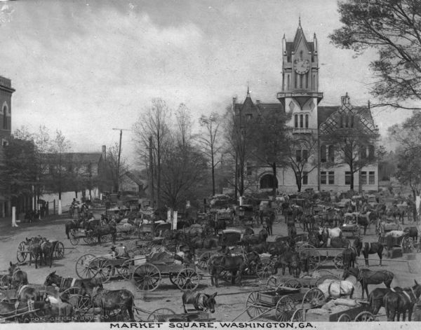 Elevated view of a number of horse-drawn carriages gathered at a market. A large clock tower is in the background. Caption reads: "Market Square, Washington, GA."