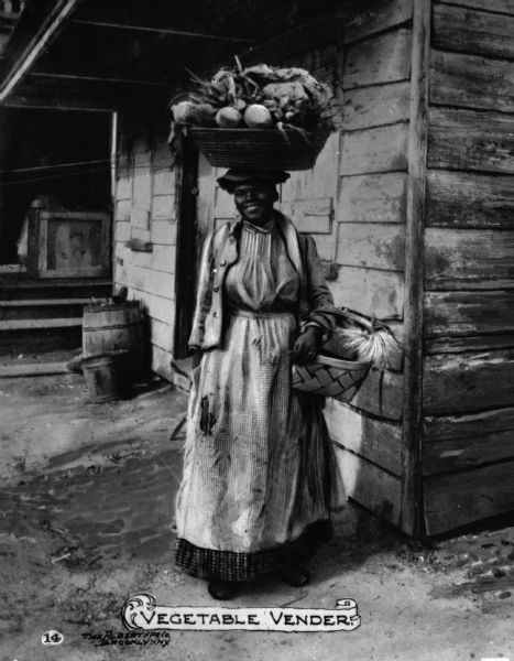 African American vegetable vendor with a large basket of vegetables balanced on her head and another in the crook of her arm. Text on photograph reads "Vegetable Vendor."