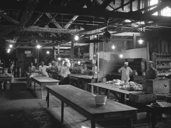 Kitchen workers in the Unity House Kitchen, a large room with long wooden tables and exposed rafters. The workers are lounging around the tables.