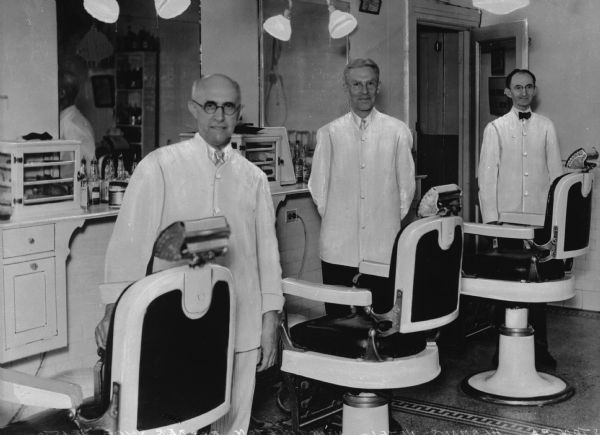 Three barbers standing proudly next to empty barber chairs at Herman's Hotel.